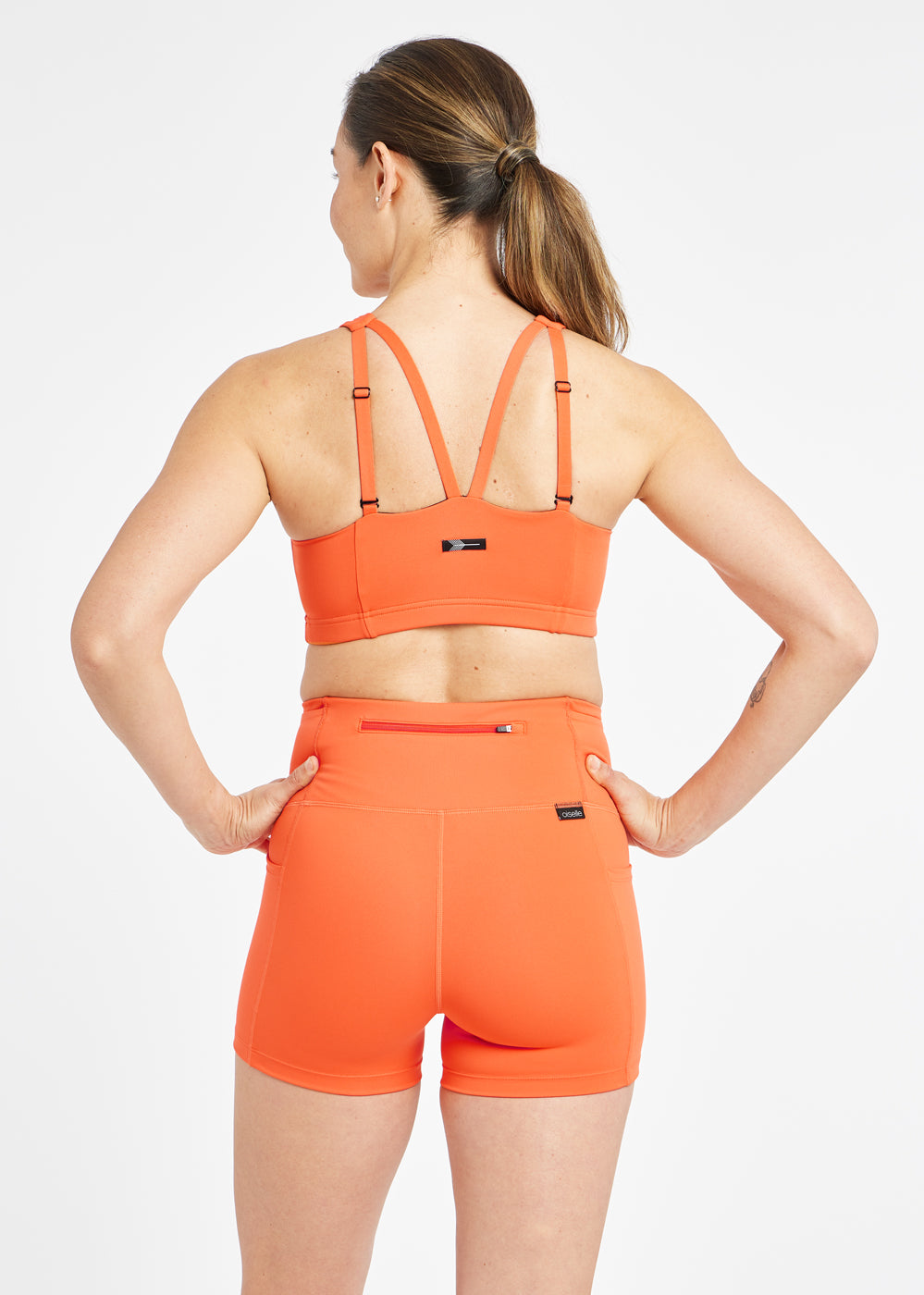 Woman wearing orange sports bra in size 6, back view