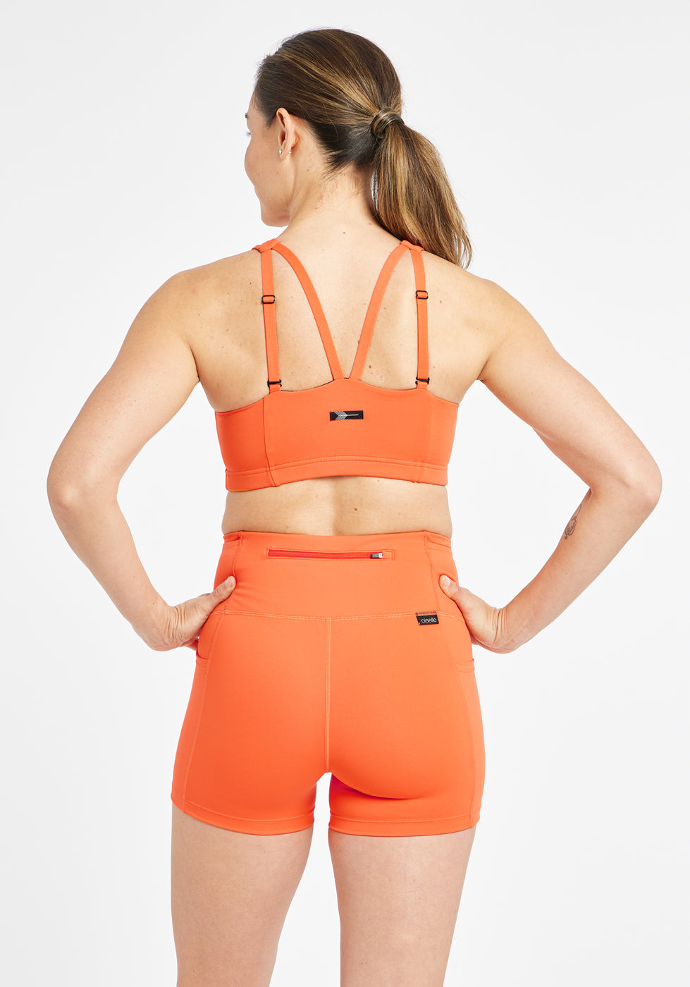 Woman wearing orange sports bra in size 6, back view