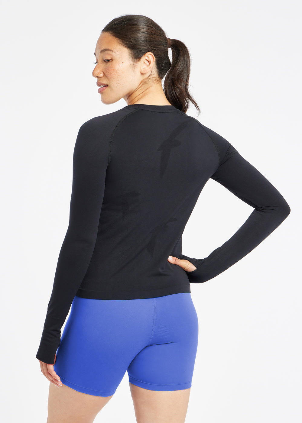 Woman wearing a black running long sleeve and blue compression shorts, back view