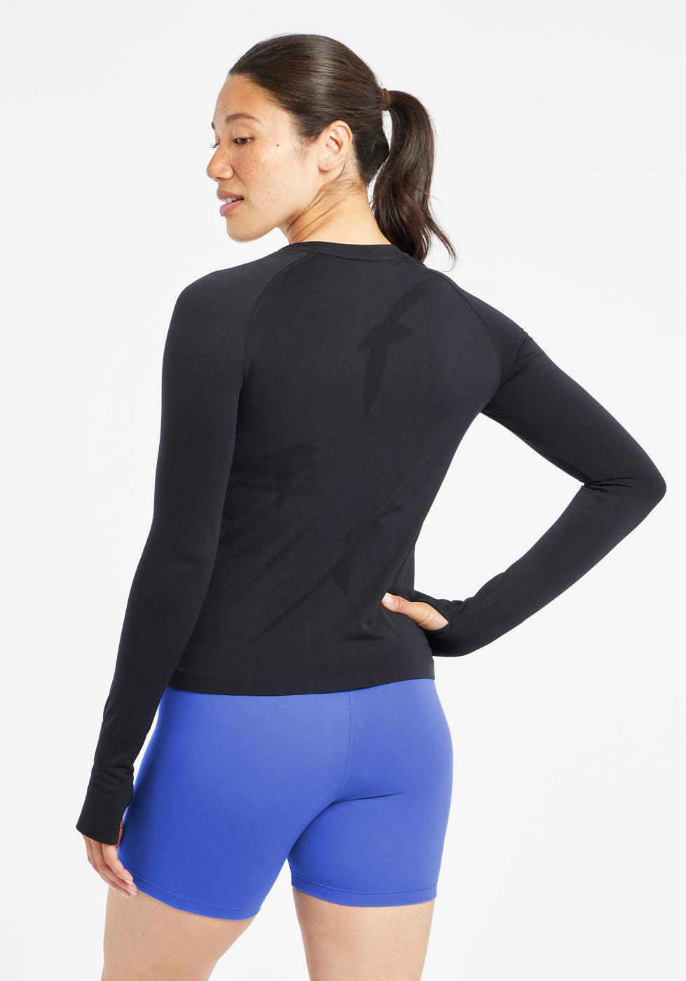 Woman wearing a black running long sleeve and blue compression shorts, back view