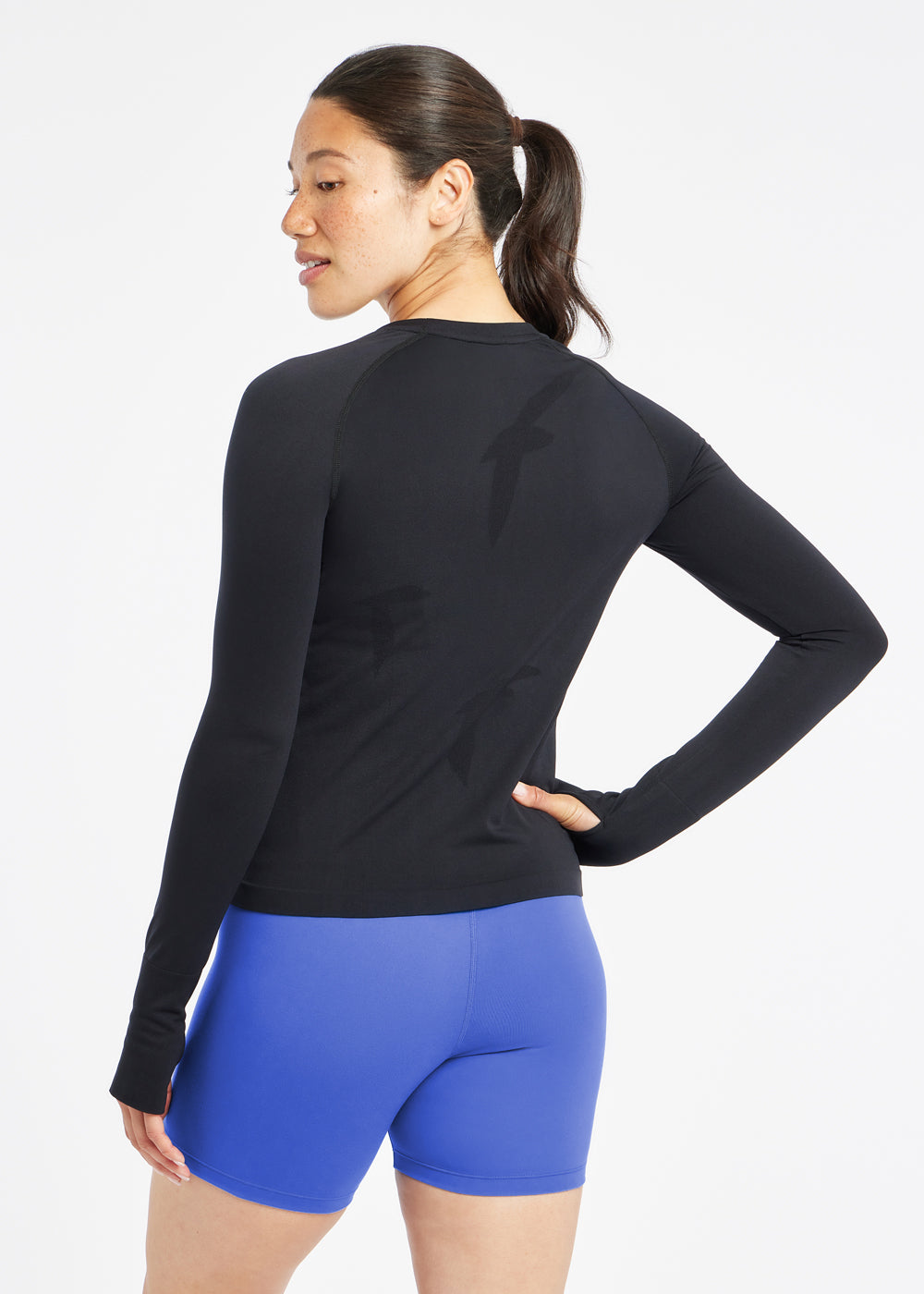 Woman wearing a black running long sleeve and blue compression shorts, back view