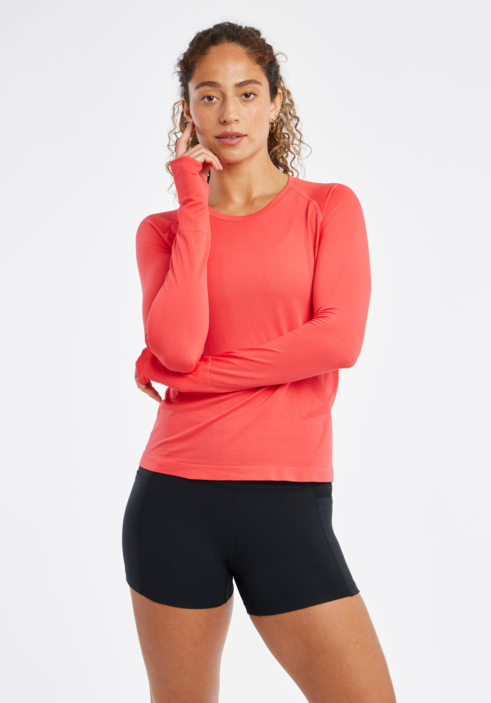 Woman wearing a red orange running long sleeve and black compression shorts, front view