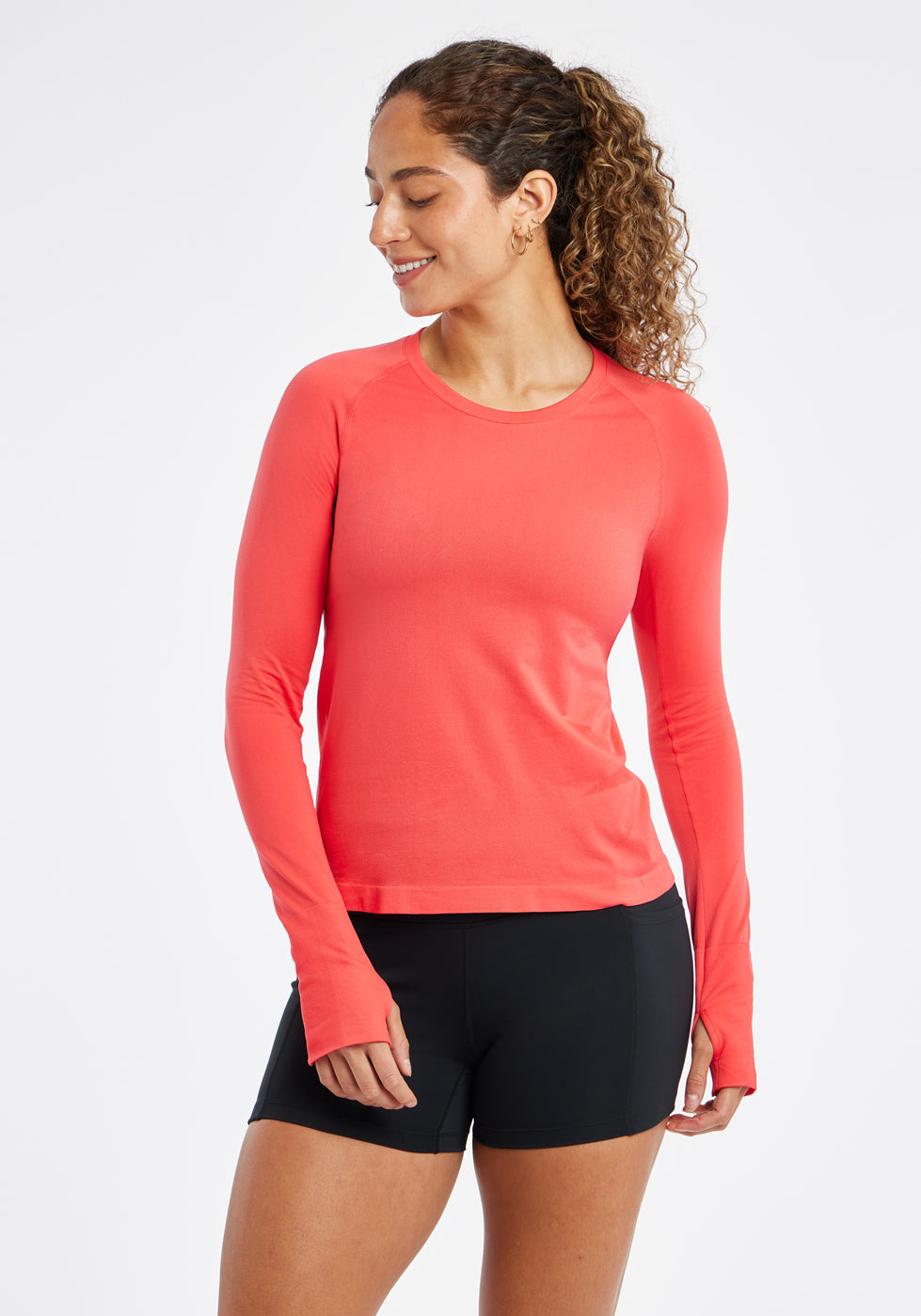 Woman wearing a red orange running long sleeve and black compression shorts, alternate front view