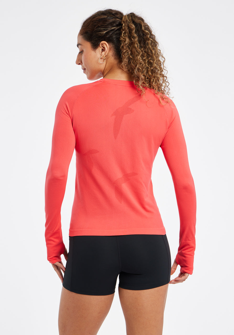 Woman wearing a red orange running long sleeve and black compression shorts, back view