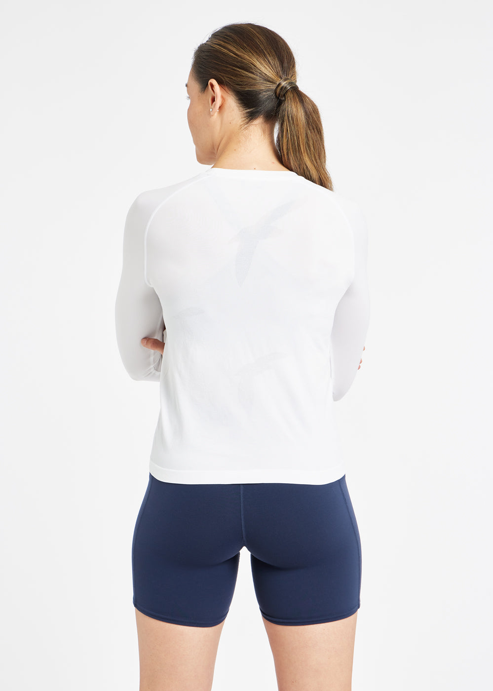 Woman wearing a white running long sleeve and blue compression shorts, back view