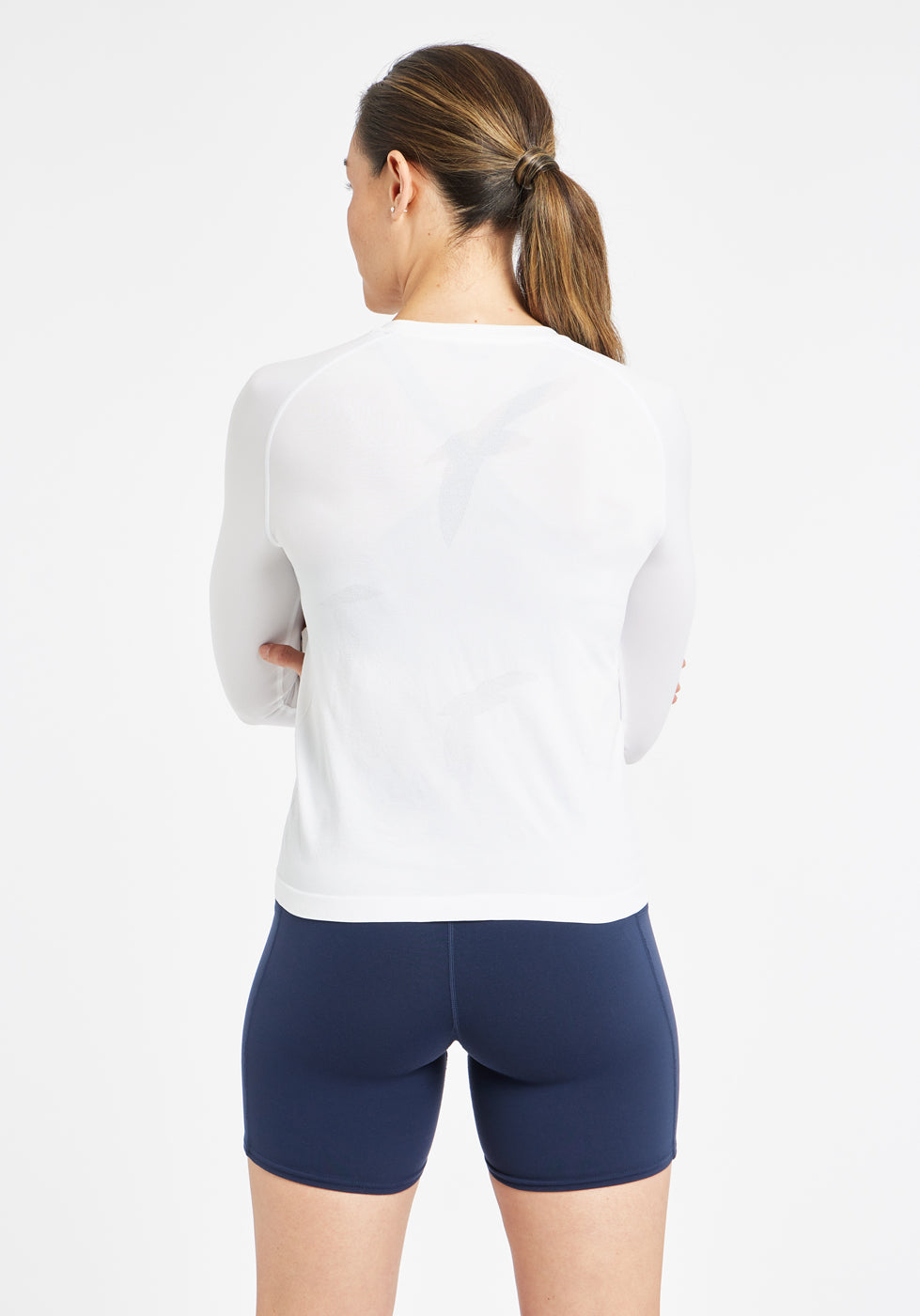 Woman wearing a white running long sleeve and blue compression shorts, back view