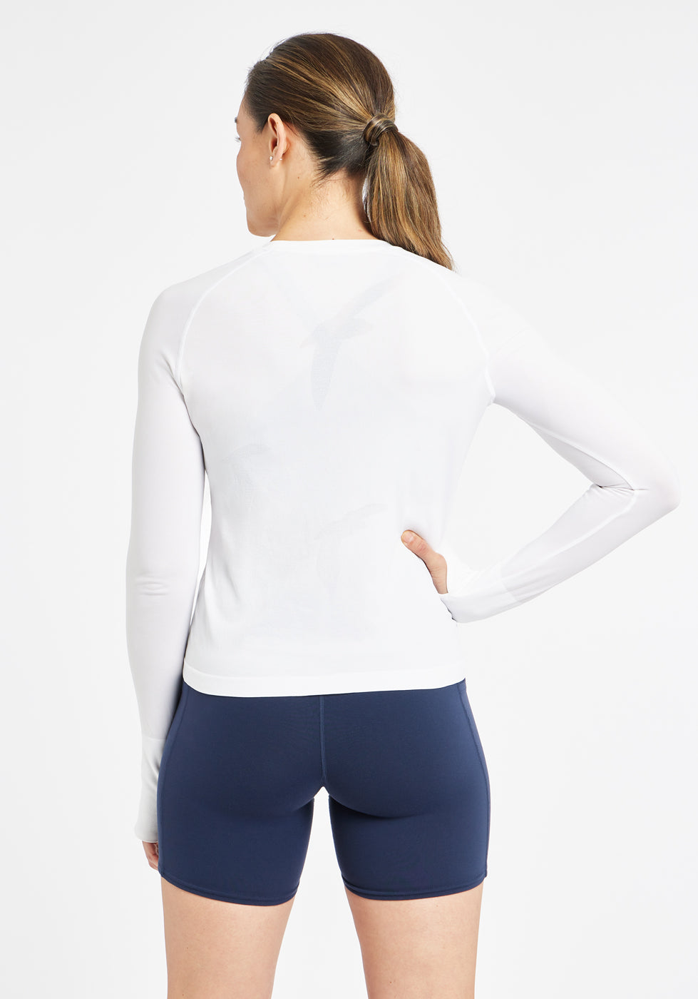 Woman wearing a white running long sleeve and blue compression shorts, alternate back view