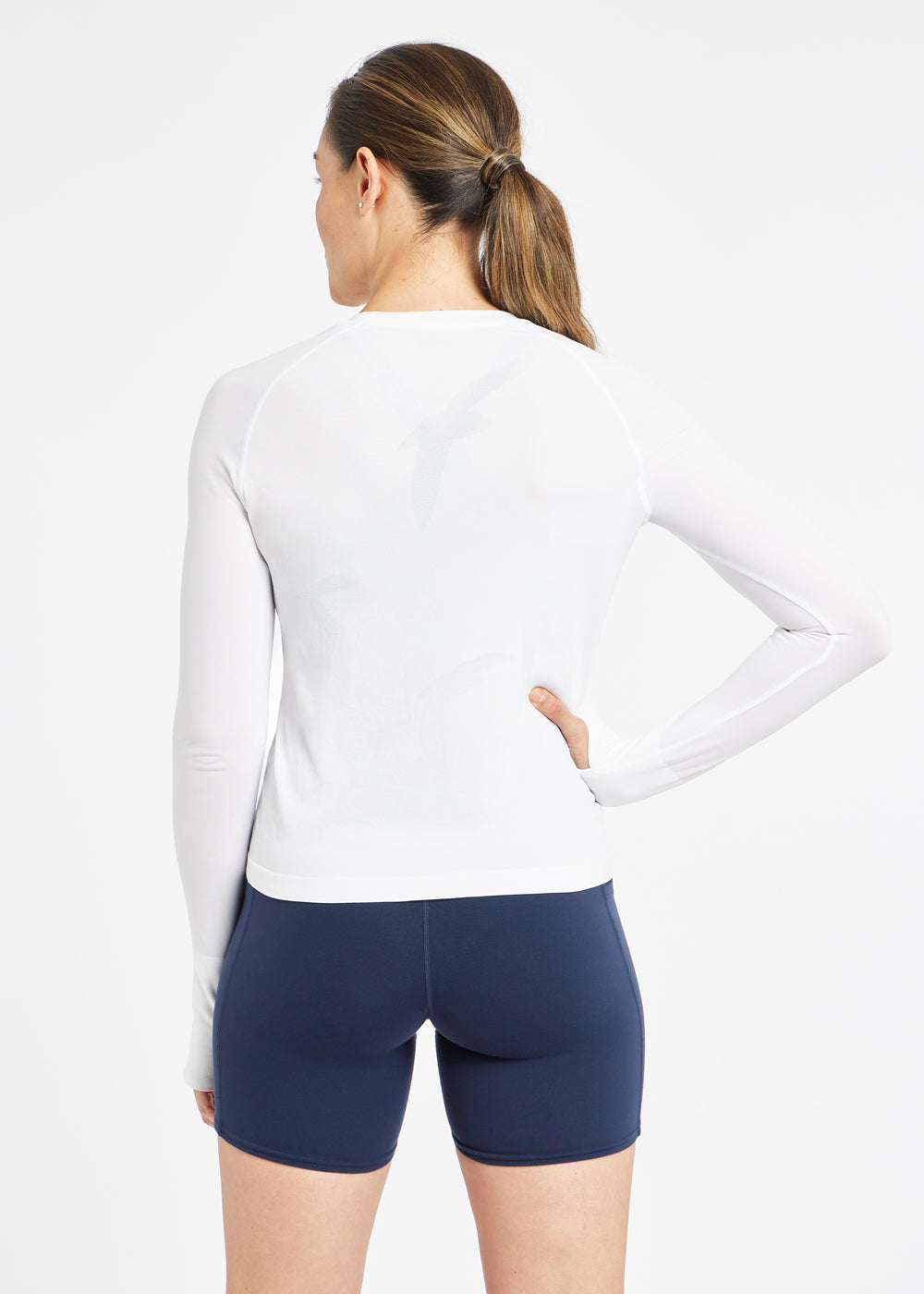 Woman wearing a white running long sleeve and blue compression shorts, alternate back view