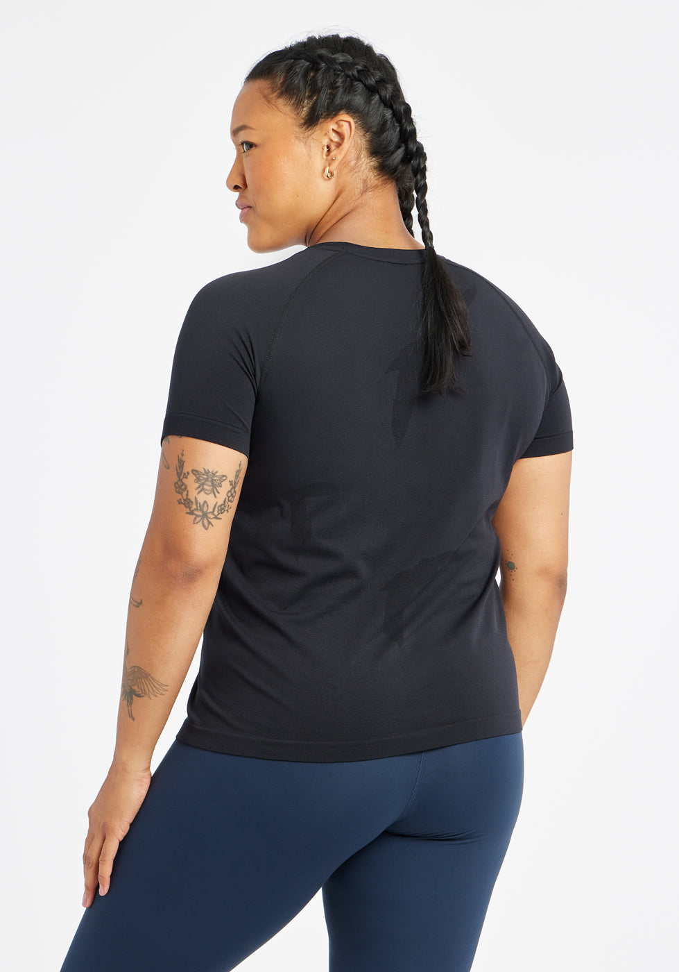 Woman wearing a black running short sleeve and navy compression tights, back view