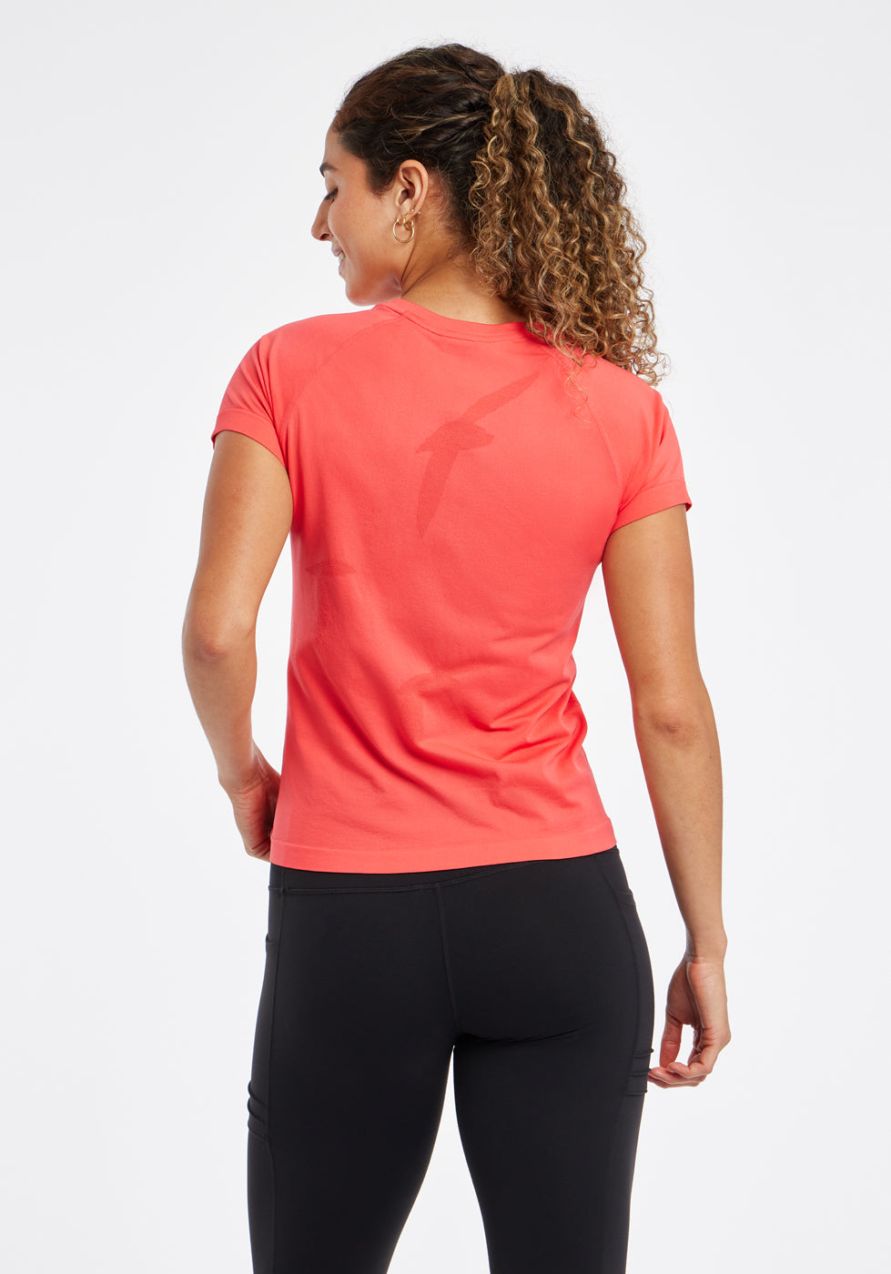 Woman wearing a red orange running short sleeve and black compression tights, back view