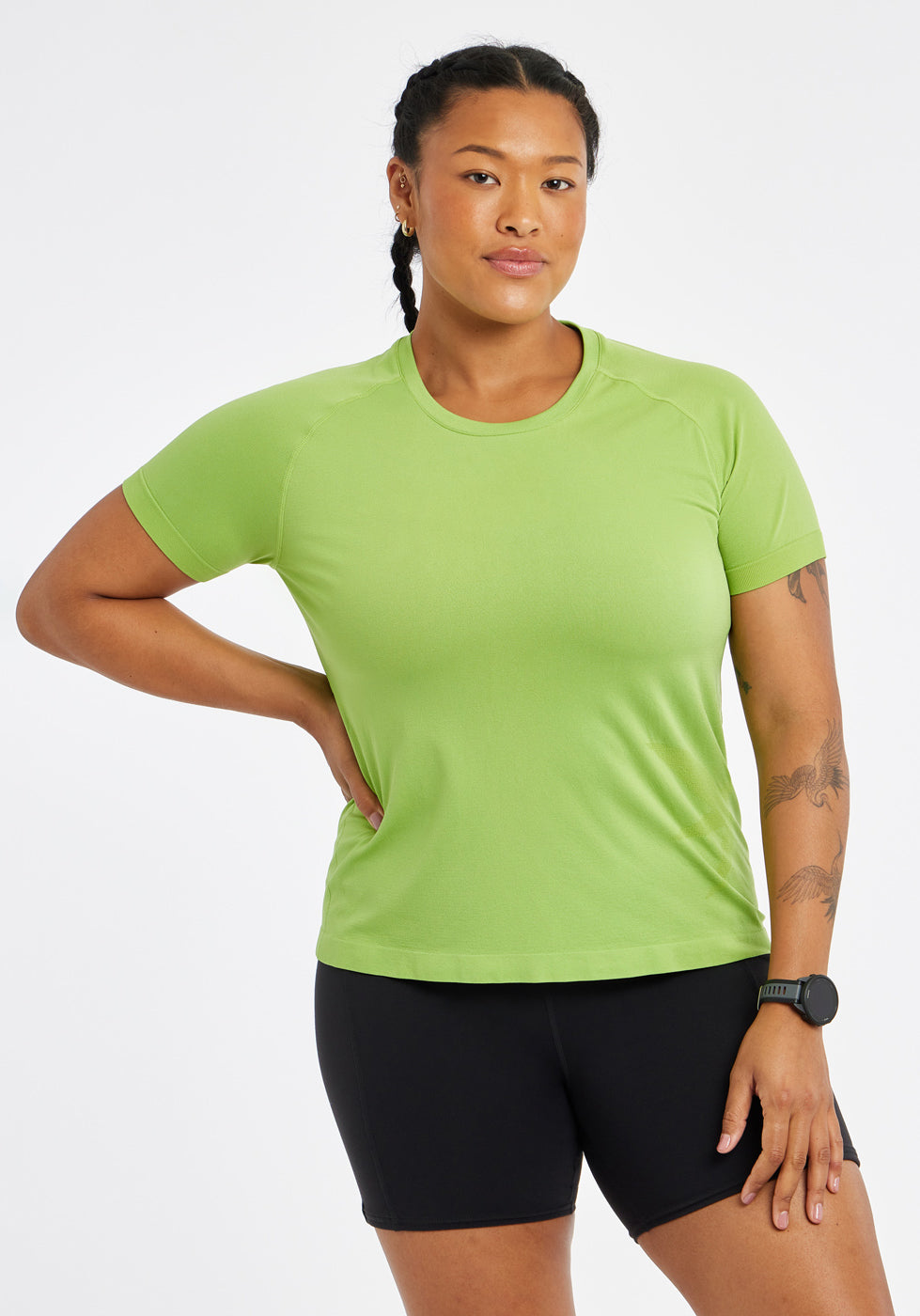 Woman wearing a green running short sleeve and black compression shorts, alternate front view