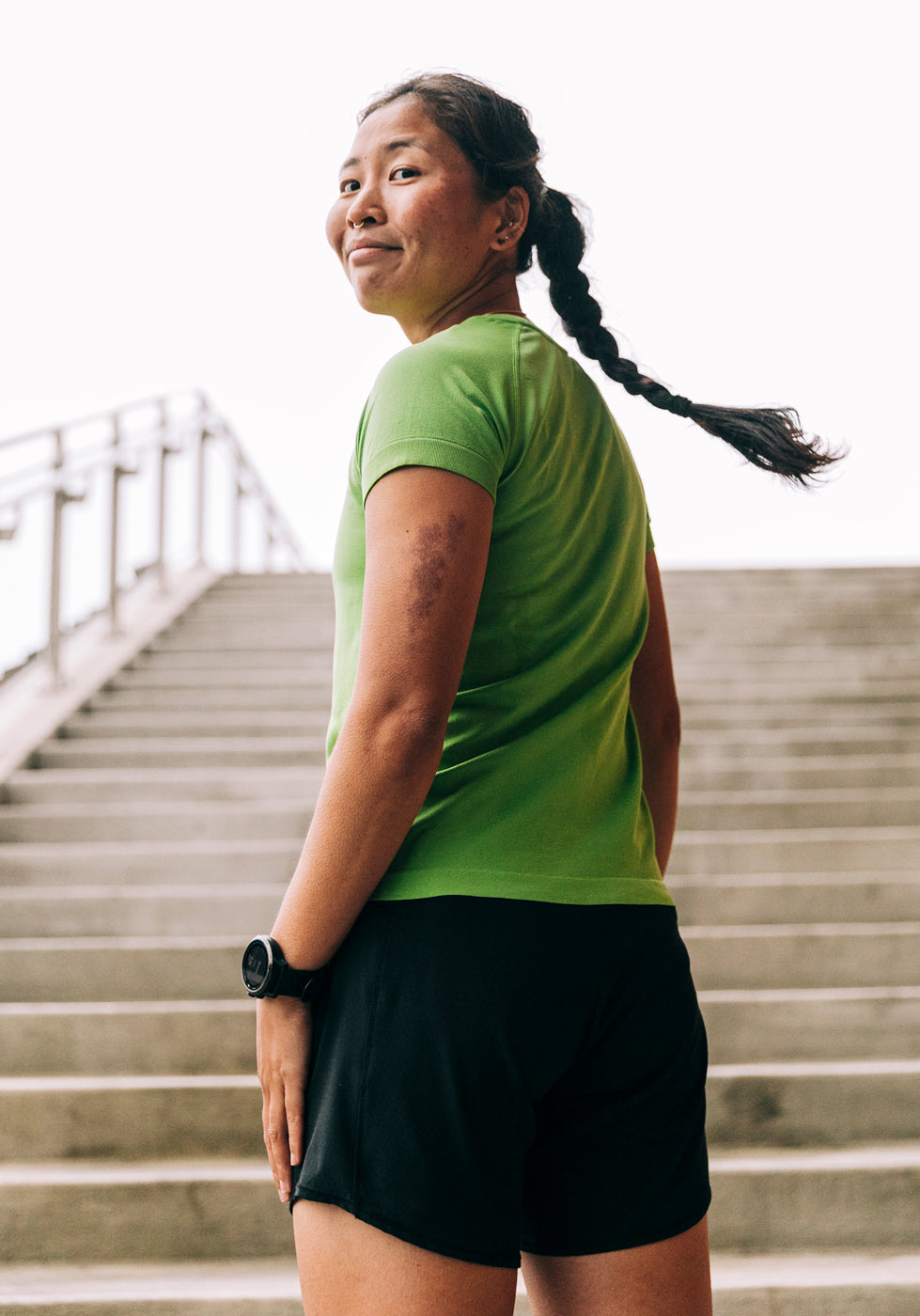 Woman wearing a green running short sleeve and black shorts, running up stairs