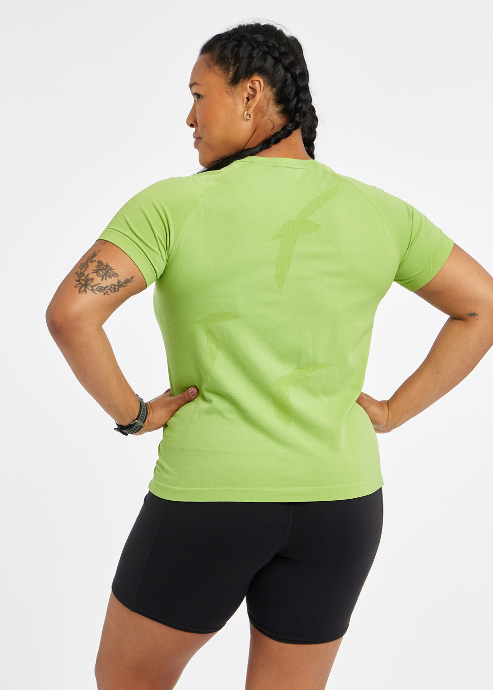 Woman wearing a green running short sleeve and black compression shorts, back view