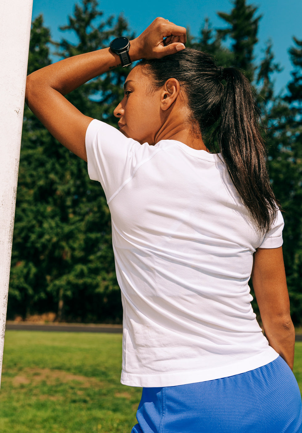Outdoor image of a woman wearing a white running short sleeve and blue shorts, back view