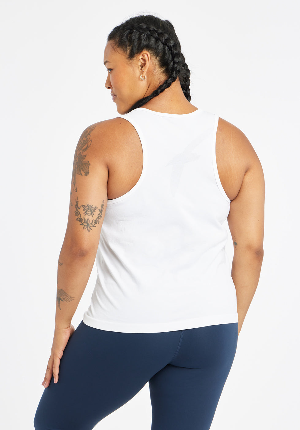 Woman wearing a white running tank top and blue compression tights, back view