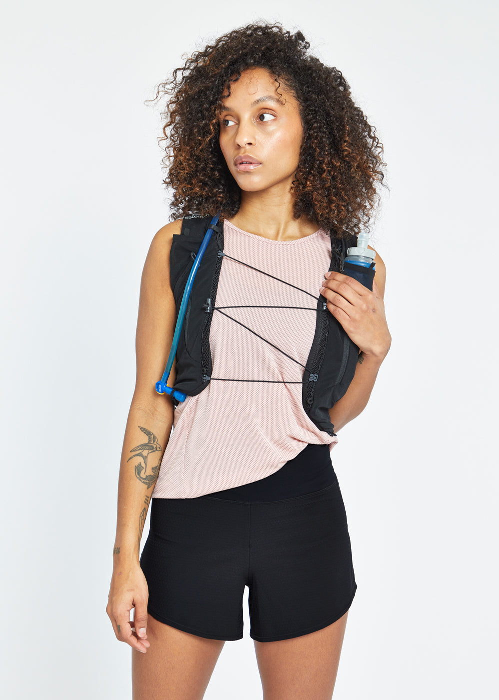 Woman wearing High Rise Roga 4" Running Shorts in black, paired with Flyout Trail Tank and hydration vest