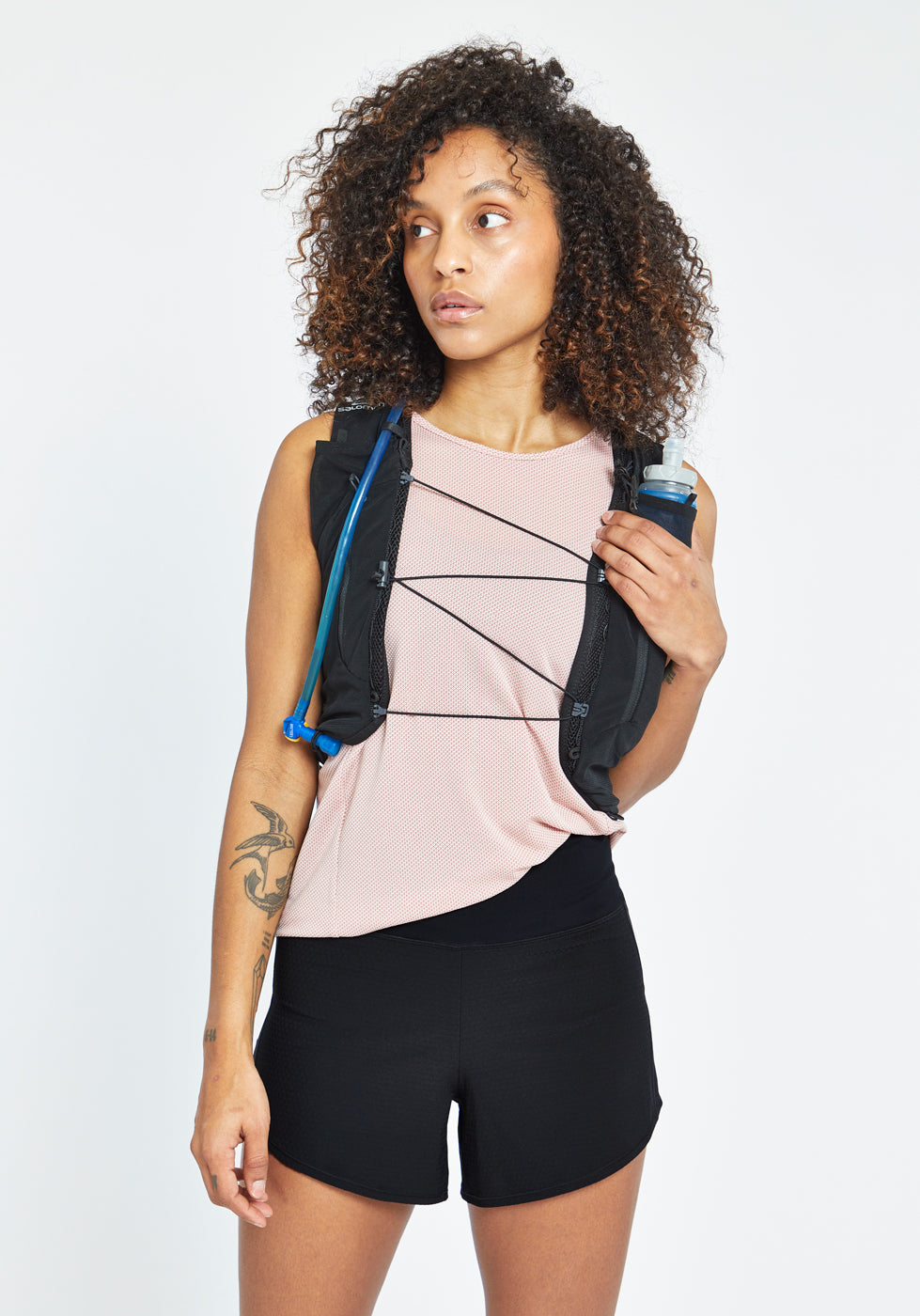 Woman wearing High Rise Roga 4" Running Shorts in black, paired with Flyout Trail Tank and hydration vest