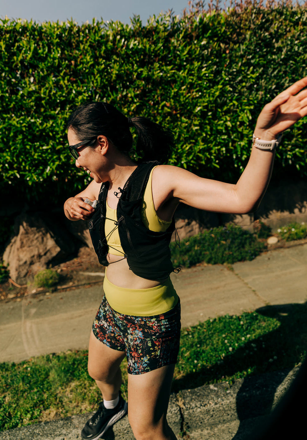 Woman running outside in High Rise Roga 4" Running Shorts in Dark Floral print and hydration vest