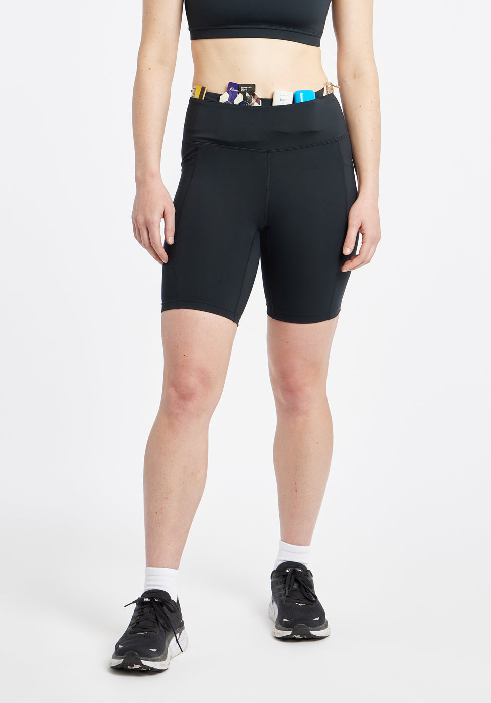 Woman wearing black compression shorts in size 6, front view with items in waistband pocket