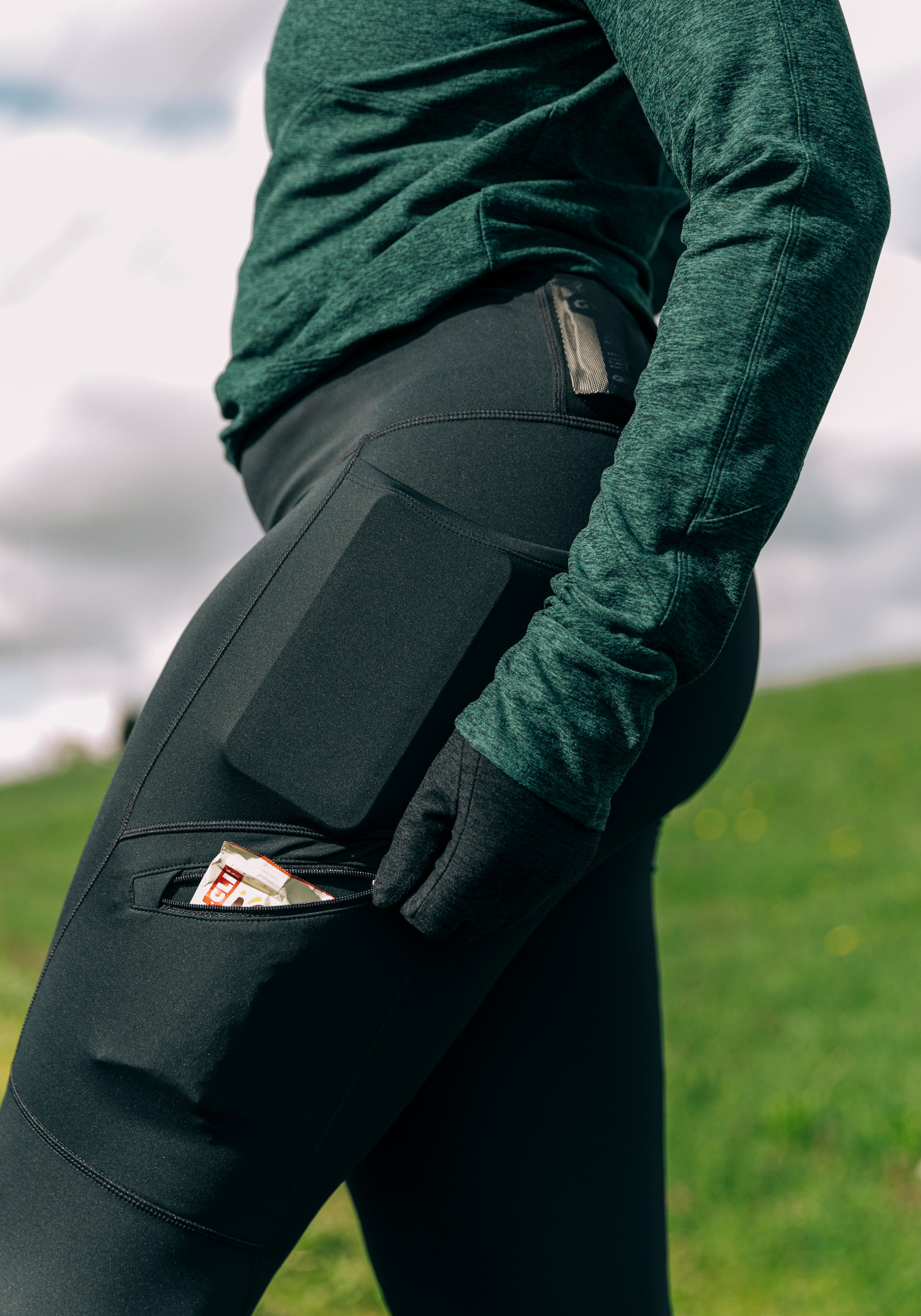 Woman wearing green top and black running tights, close up detail of running gel in side pocket