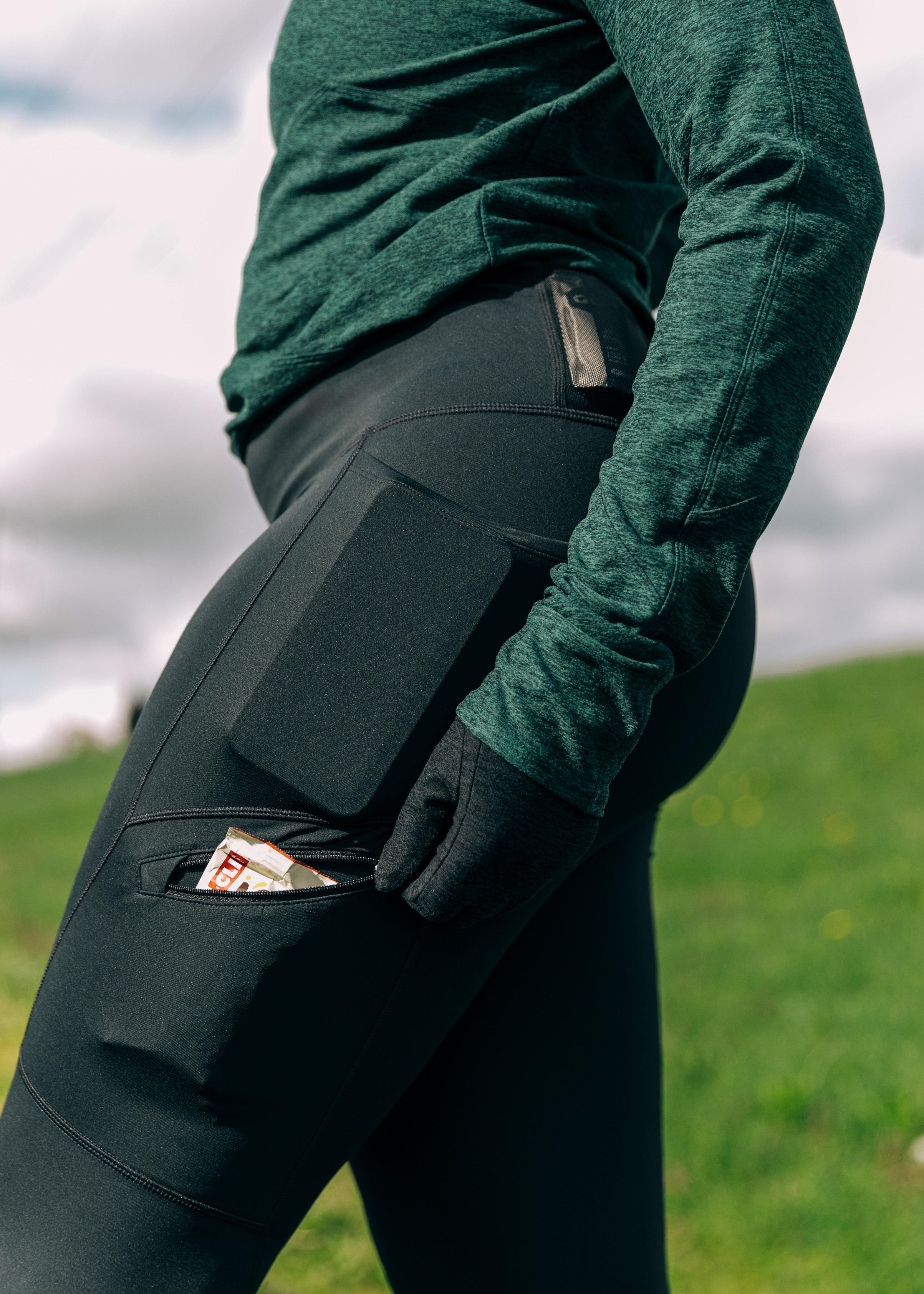 Woman wearing green top and black running tights, close up detail of running gel in side pocket