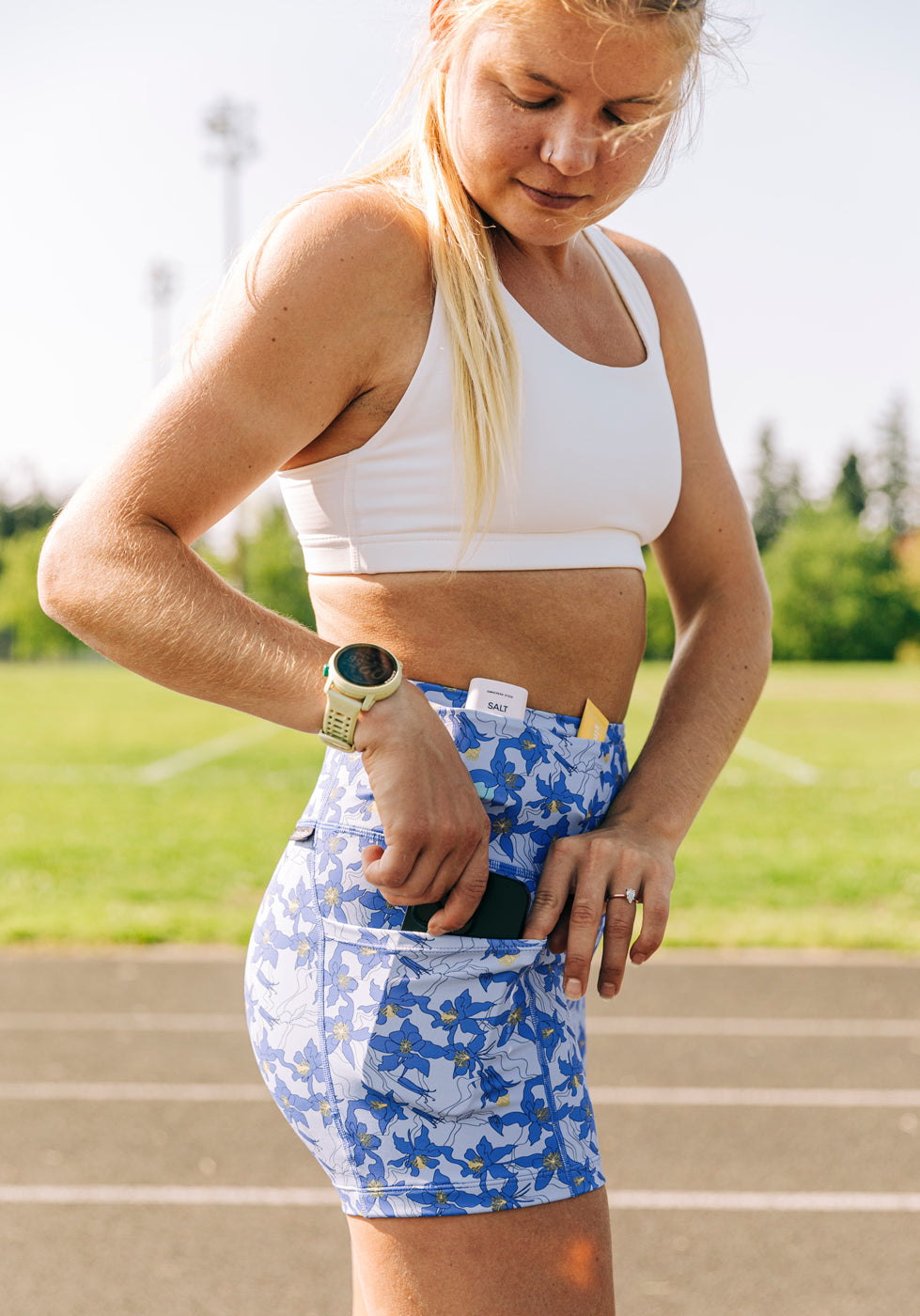 Allie Ostrander on a track wearing white Oiselle sports bra and blue with blue flower print compression shorts