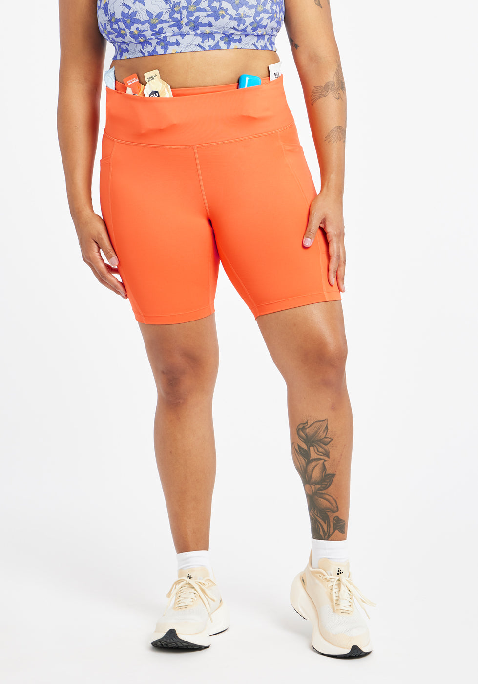Woman wearing orange compression shorts in size 12, front view with items in waistband pocket