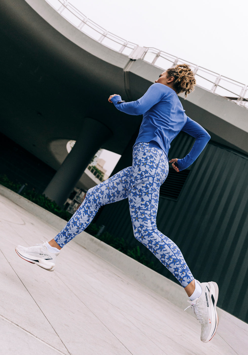 Woman running outside in a blue long sleeve and blue with blue flower print running tights