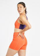Woman wearing orange and purple paneled sports bra, side view