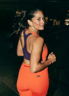 Woman in matching Oiselle orange and purple paneled sports bra and shorts running at night