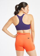 Woman wearing orange and purple paneled sports bra, alternate back view