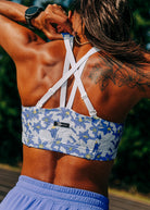 Woman wearing blue with blue floral print sports bra, close up back view outside on a track