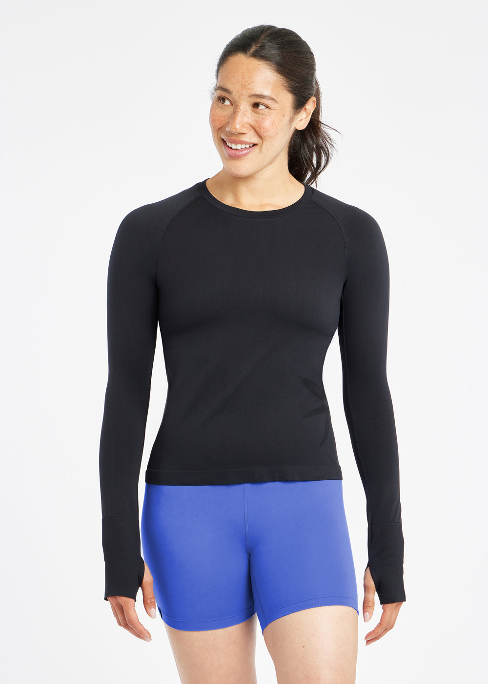 Woman wearing a black running long sleeve and blue compression shorts, alternate front view