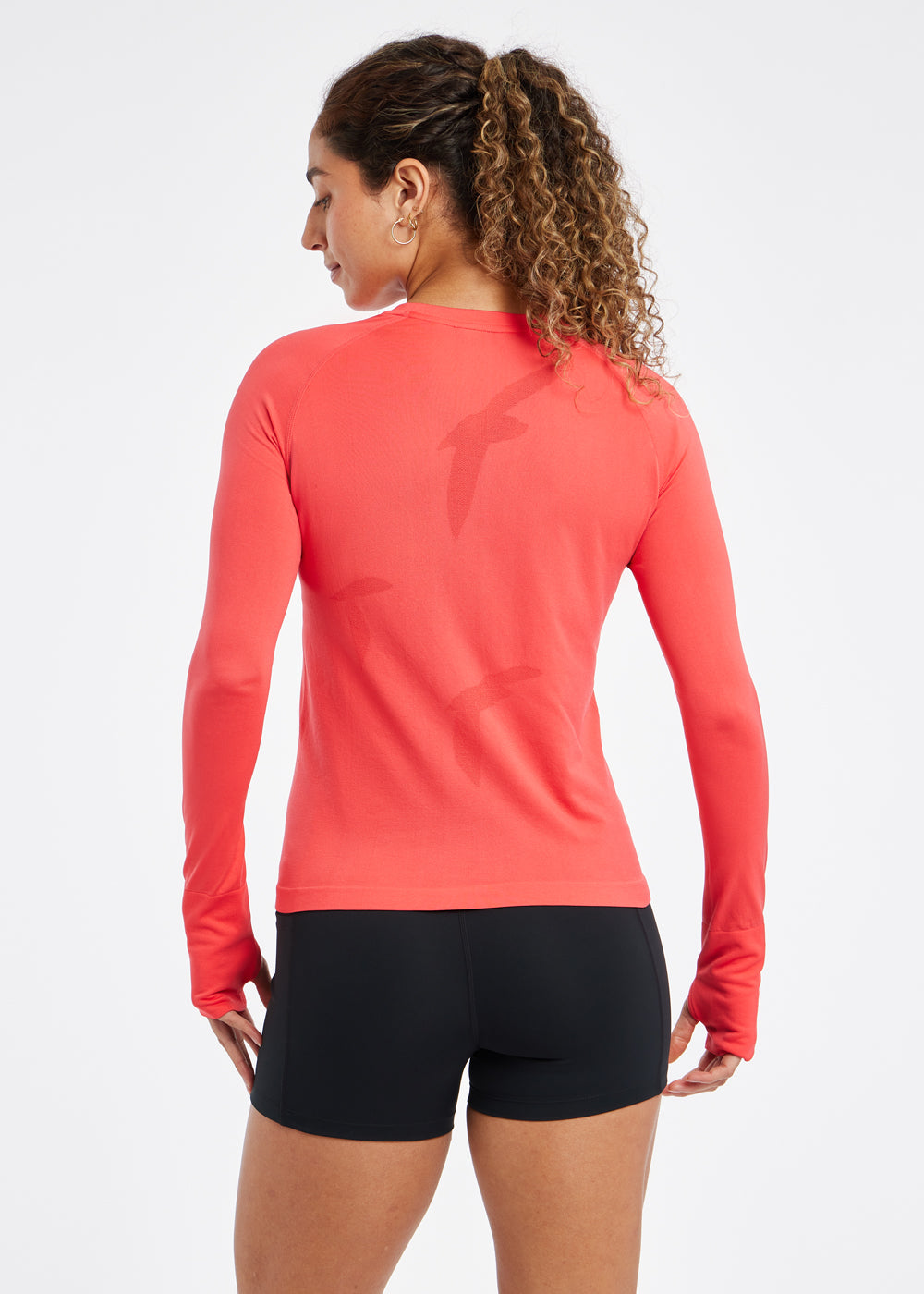Woman wearing a red orange running long sleeve and black compression shorts, back view