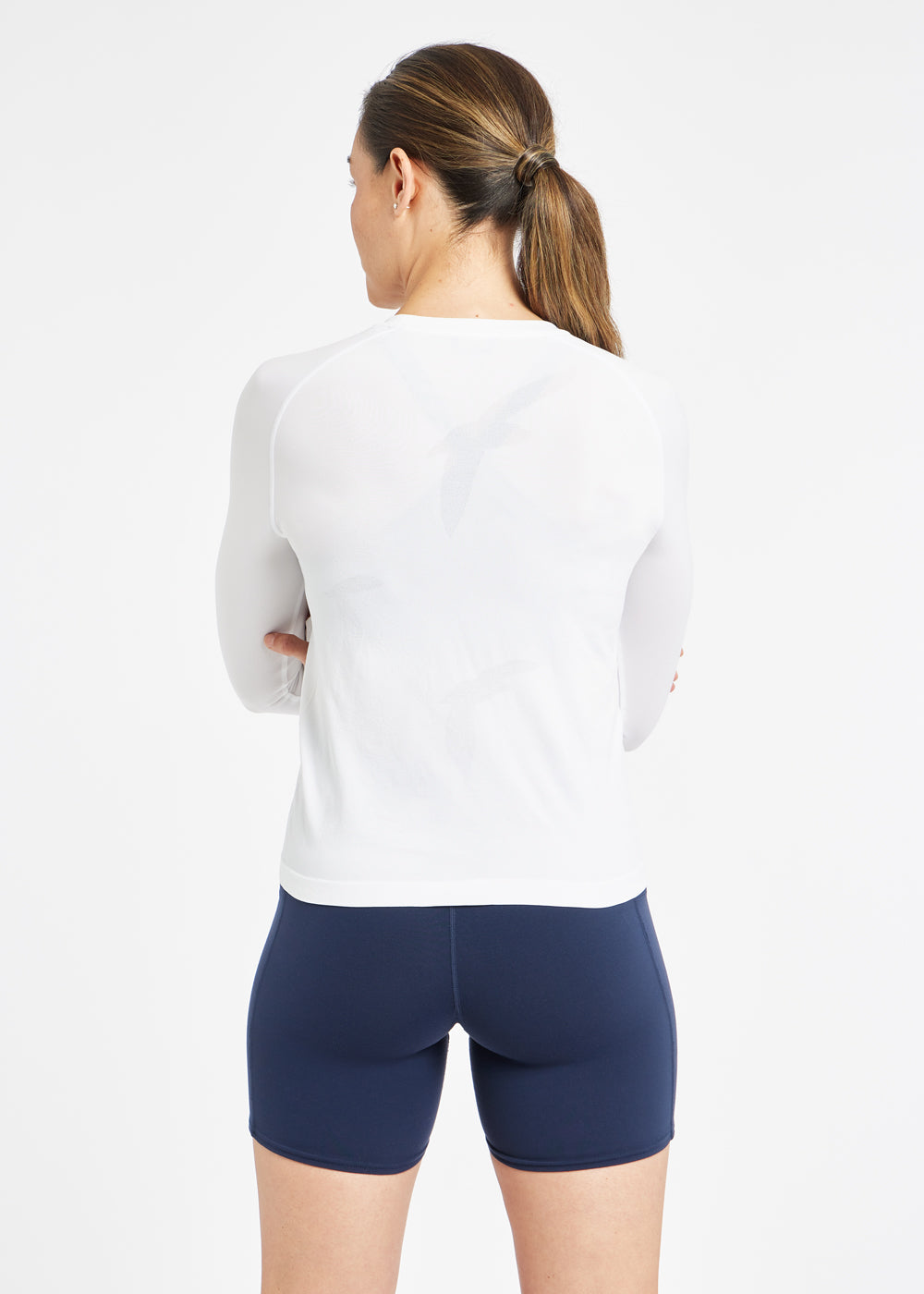 Woman wearing a white running long sleeve and blue compression shorts, back view