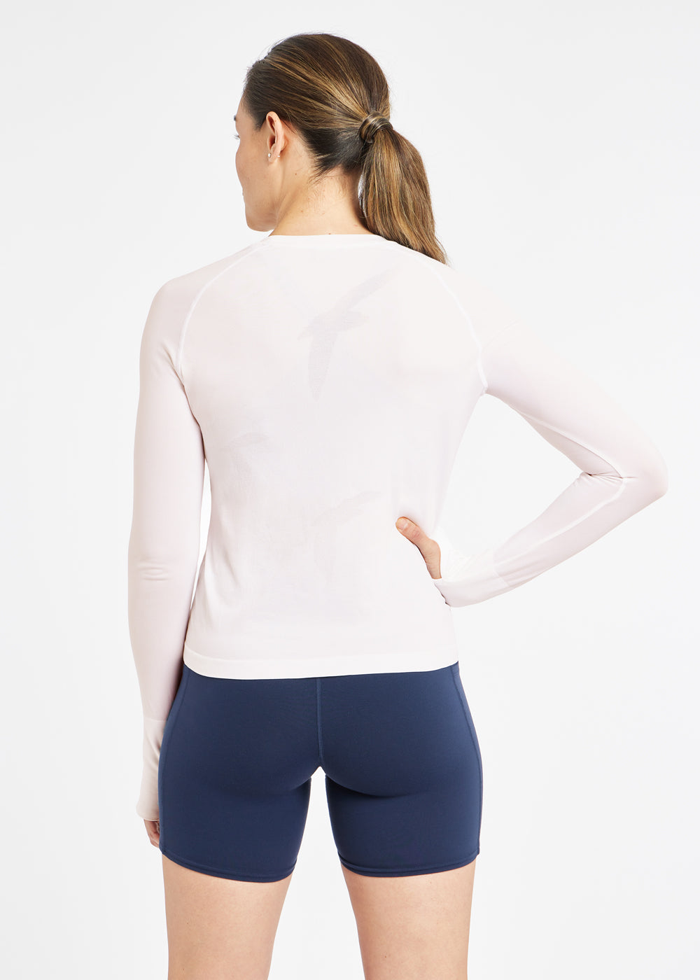 Woman wearing a white running long sleeve and blue compression shorts, back view
