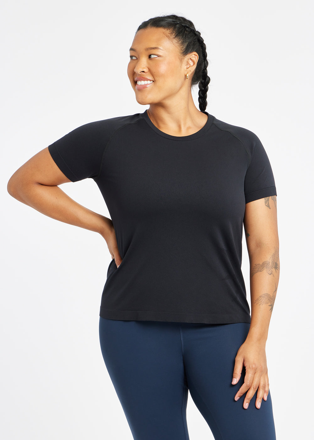 Woman wearing a black running short sleeve and navy compression tights, alternate front view