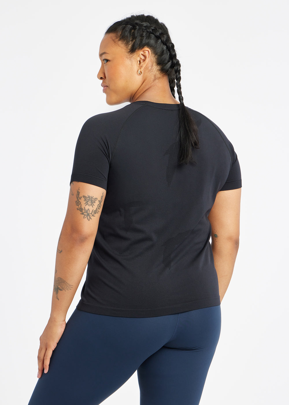 Woman wearing a black running short sleeve and navy compression tights, back view