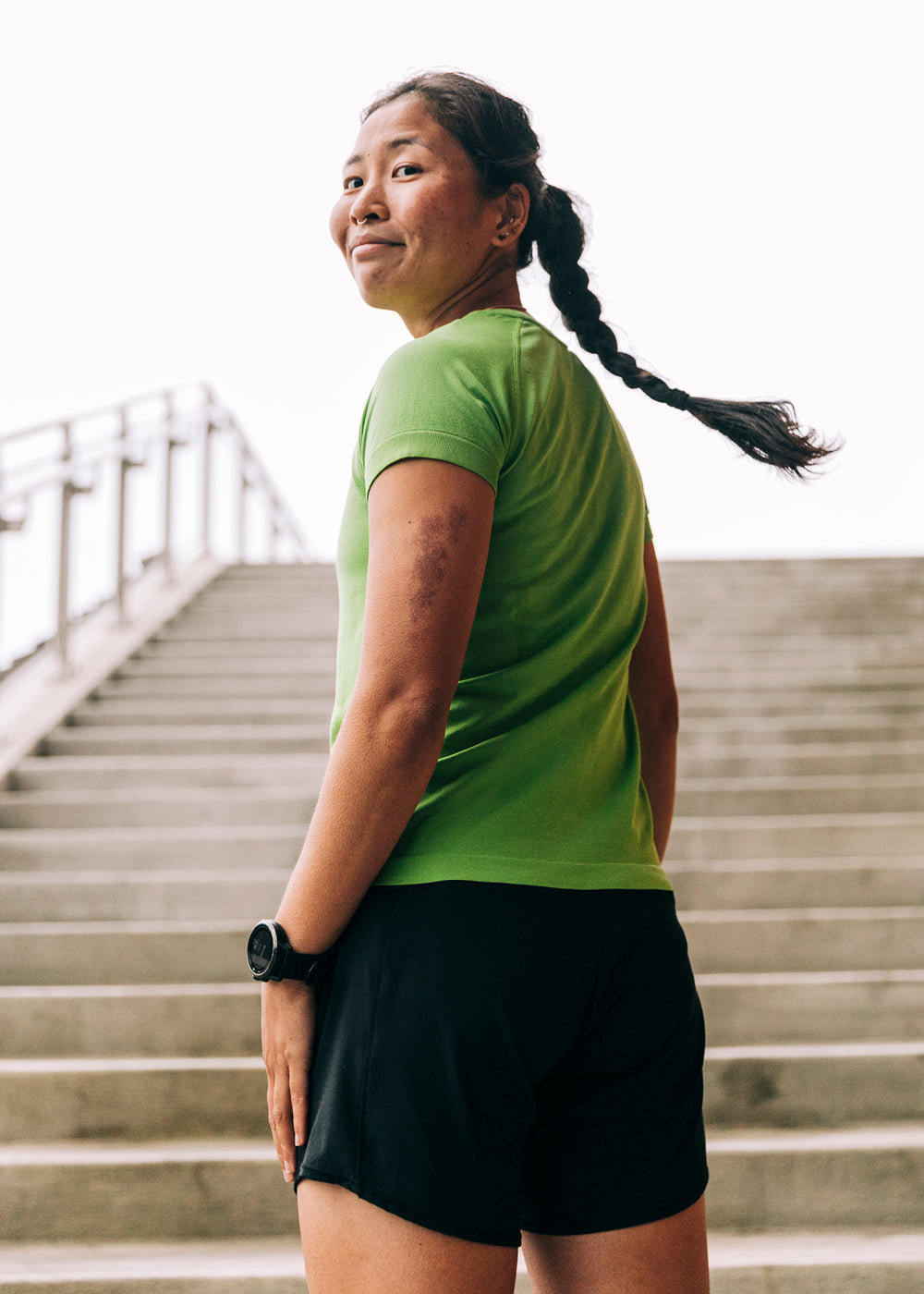 Woman wearing a green running short sleeve and black shorts, running up stairs