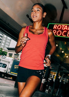 Woman wearing a red orange running tank top and black compression shorts, running through Pike Place Market
