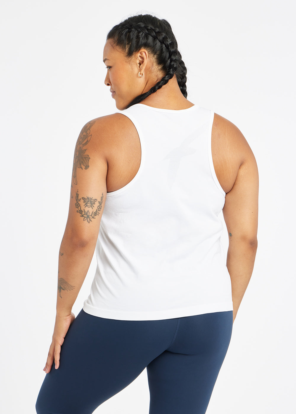Woman wearing a white running tank top and blue compression tights, back view