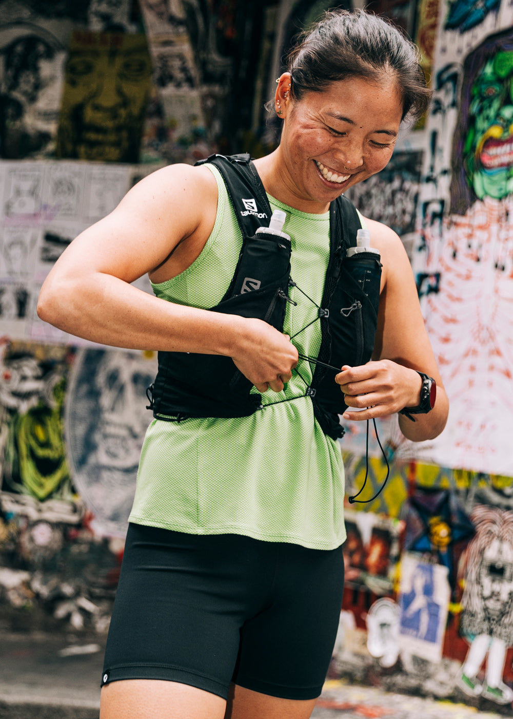 Flyout Trail Tank in Green Limelight with trail running pack, running in city alleyway