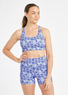 Woman wearing matching blue with blue flower print sports bra and compression shorts in size 6, alternate front view