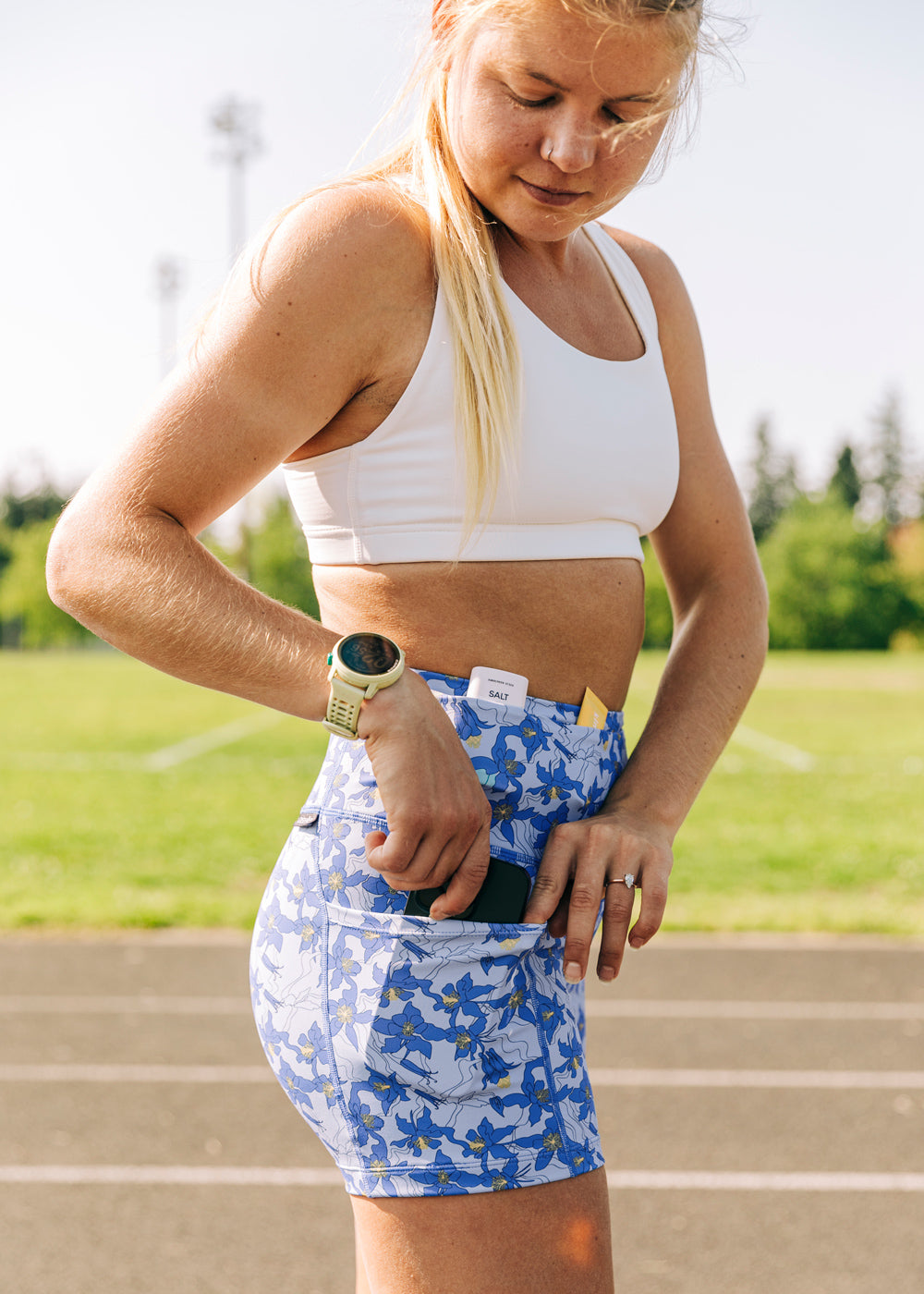 Allie Ostrander on a track wearing white Oiselle sports bra and blue with blue flower print compression shorts