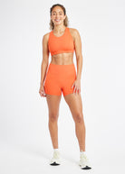 Woman wearing matching orange sports bra and compression shorts in size 6, front view