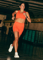 Woman running in matching orange Oiselle sports bra and compression shorts