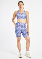 Woman wearing matching blue with blue floral print sports bra and compression shorts in size 6, front view