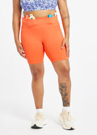 Woman wearing orange compression shorts in size 12, front view with items in waistband pocket